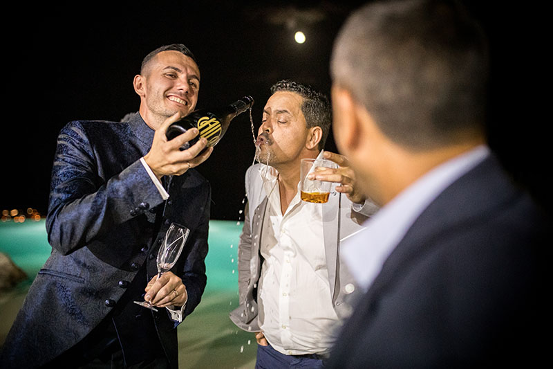 sposo che fa bere direttamente dalla bottiglia un invitato. Scatto di Mario Amelio Fotografo di matrimonio reportage.