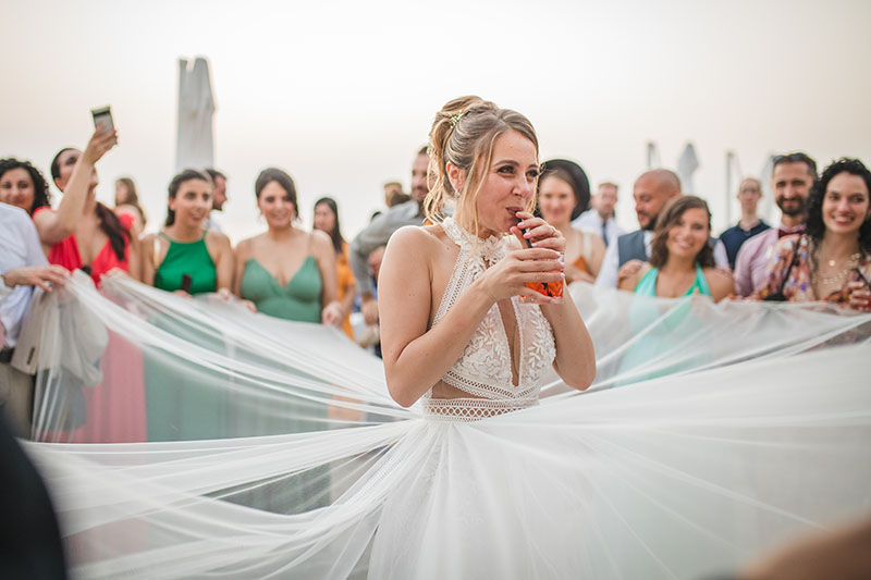 sposa che beve lo spritz mentre le invitate le alzano il velo. Scatto di Mario Amelio Fotografo di matrimonio reportage.