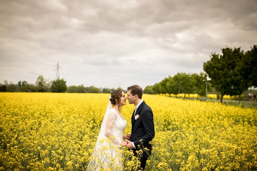 Sposi felici in un campo di colza immortalati dal fotografo matrimonio Bergamo, circondati da fiori gialli in un paesaggio suggestivo.