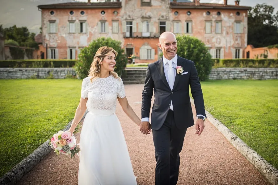 Sposi che passeggiano nei giardini di Villa Malliana a Bergamo, sorridenti e felici dopo la cerimonia facendo le foto con fotografo matrimonio bergamo.
