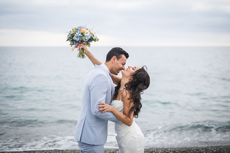 Coppia di sposi felici che si abbracciano sulla spiaggia con lo sfondo del mare, un esempio di come scegliere il fotografo di matrimonio perfetto.