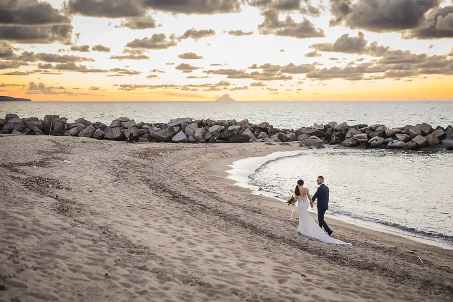Fotografo matrimonio Catanzaro: sposi che camminano mano nella mano sulla spiaggia al tramonto, con il mare sullo sfondo