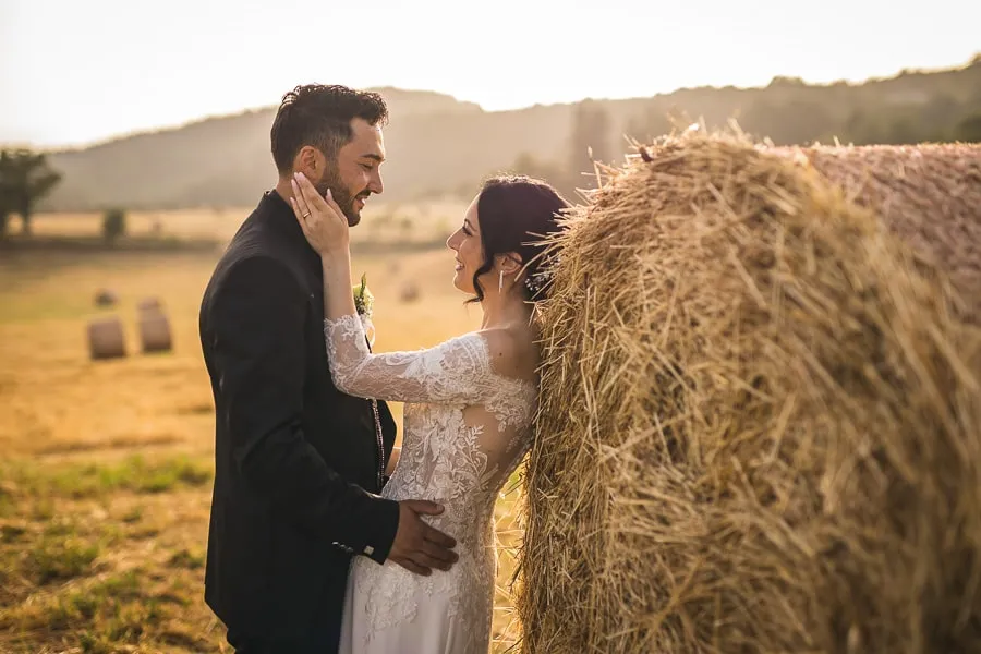 Sposi innamorati si guardano negli occhi accanto a una balla di fieno, immersi nella luce dorata del tramonto, un perfetto esempio di servizio fotografico matrimonio Catanzaro.