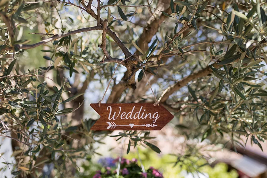 Cartello in legno con la scritta "Wedding" appeso a un ramo di ulivo, simbolo dell'importanza di un wedding planner vantaggi per l'organizzazione perfetta.