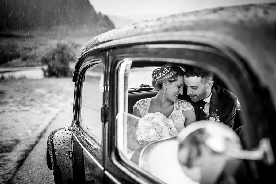 Coppia di sposi rifugiata nella macchina d’epoca durante la pioggia, situazione tipica risolta grazie alla gestione imprevisti matrimonio