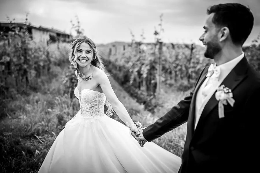 Gli sposi camminano felici tra le vigne in uno scatto naturale da reportage matrimonio Brescia