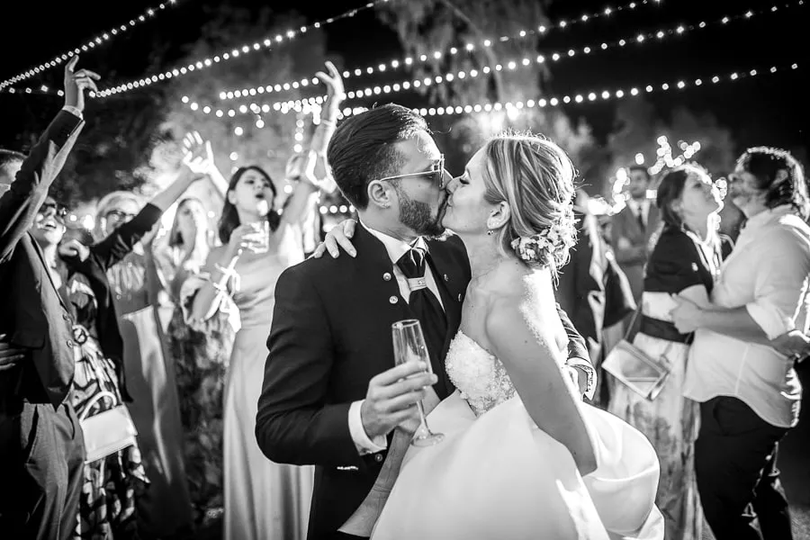 Sposi che si baciano circondati dagli amici durante la festa serale, simbolo di un reportage matrimonio Catanzaro spontaneo e coinvolgente