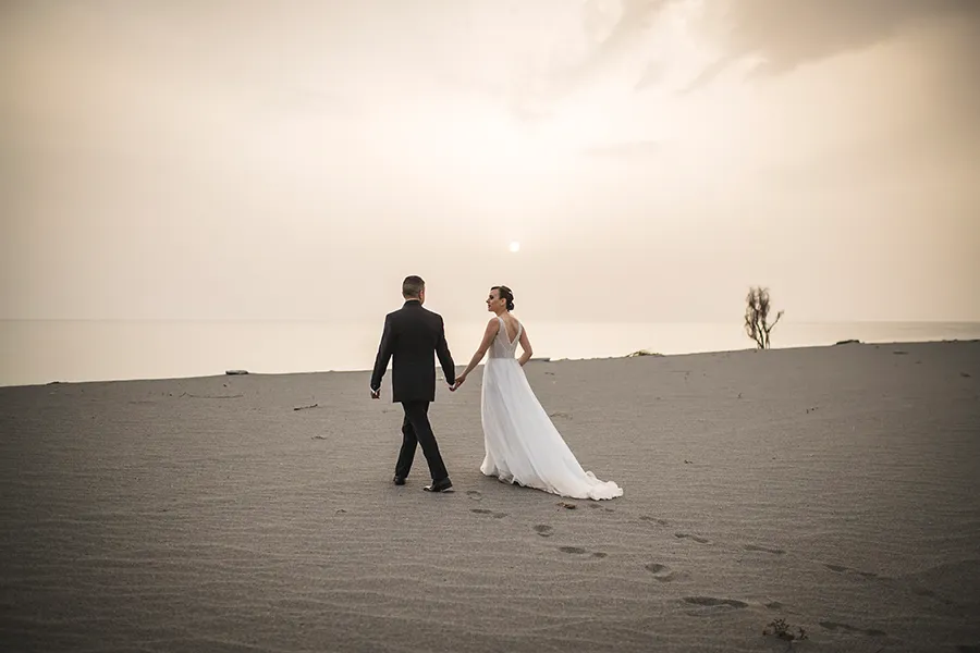Coppia di sposi cammina sulla sabbia al tramonto, esempio di una romantica location matrimonio Catanzaro con vista sul mare.