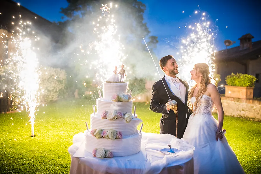 Sposi durante il taglio della torta con spettacolo pirotecnico, un momento clou da considerare nella preparazione del servizio fotografico di matrimonio a Brescia