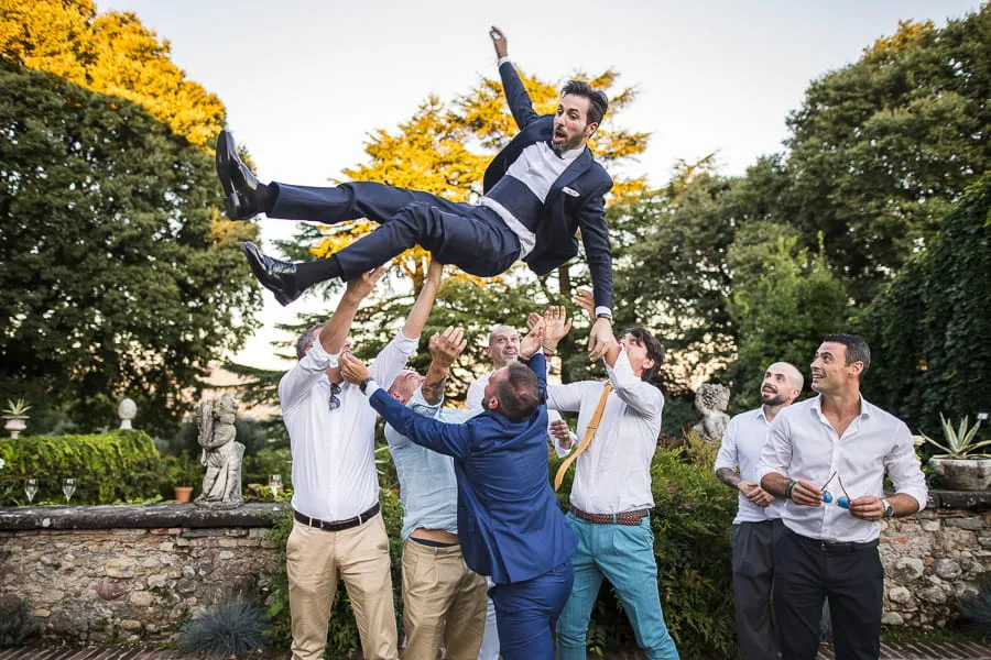 Amici lanciano lo sposo in aria durante il ricevimento, scena tipica delle tendenze fotografia matrimonio Brescia