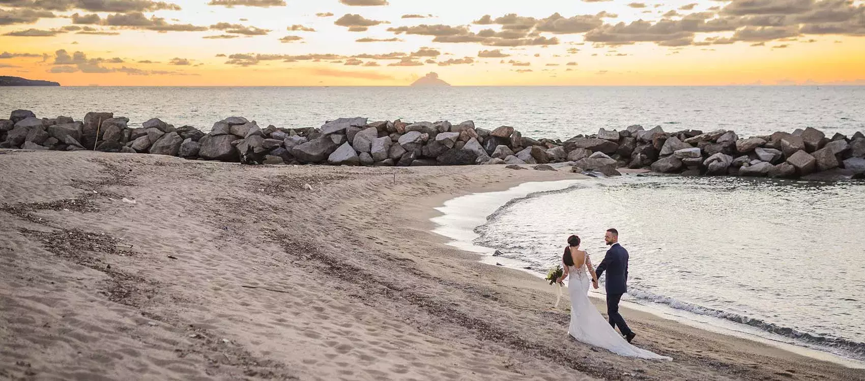 sposi che camminano sulla piaggia con lo sfondo del vulcano